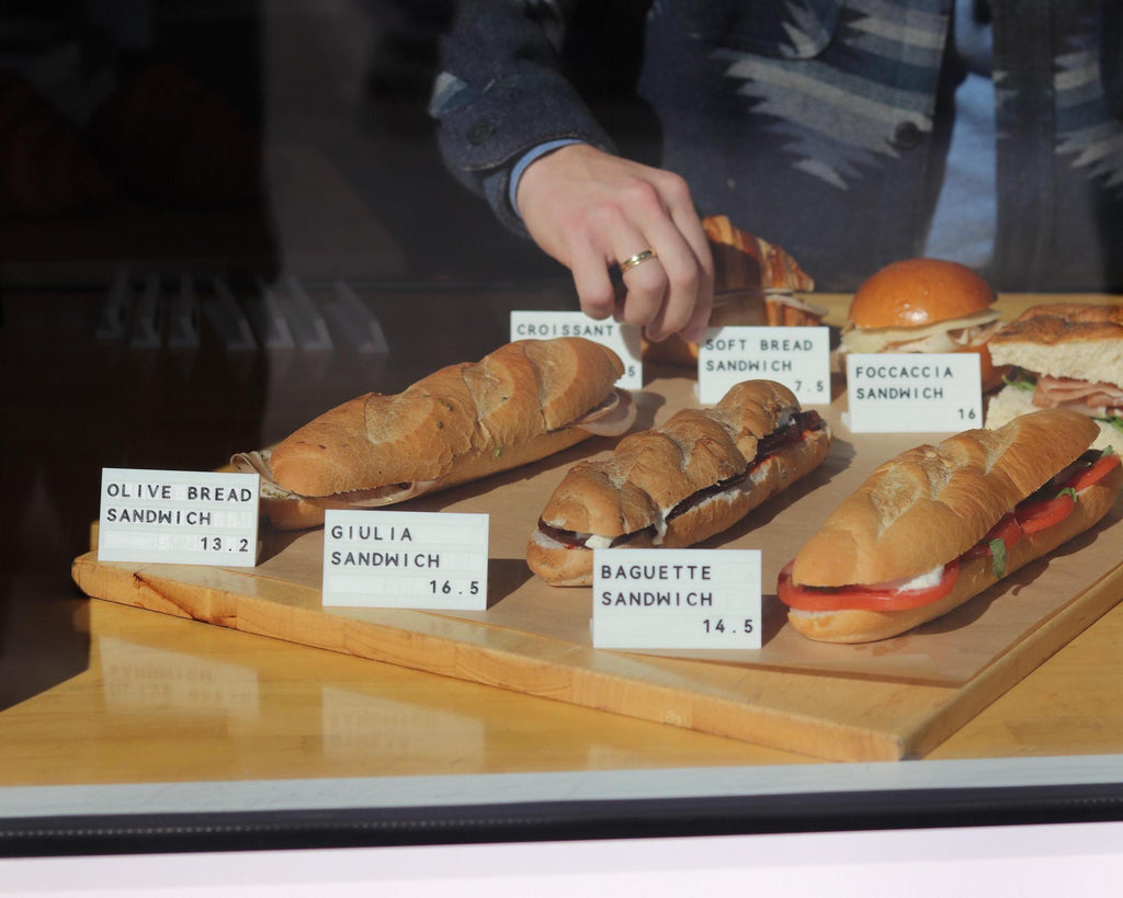 Hand arranging LettrBoard counter signs in a bakery case of baguettes