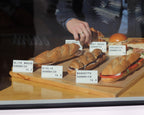 Hand arranging LettrBoard counter signs in a bakery case of baguettes