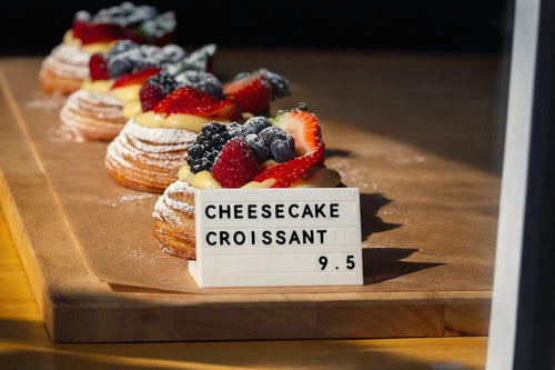 LettrBoard three-row counter sign reading CHEESECAKE CROISSANT 5.5 beside fruit pastries