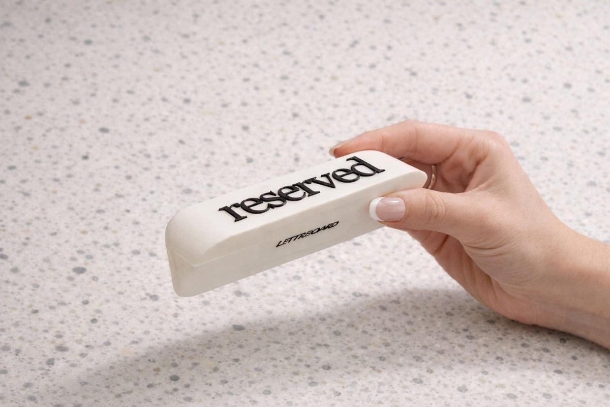 Hand placing a LettrBoard reserved table sign with raised black lettering