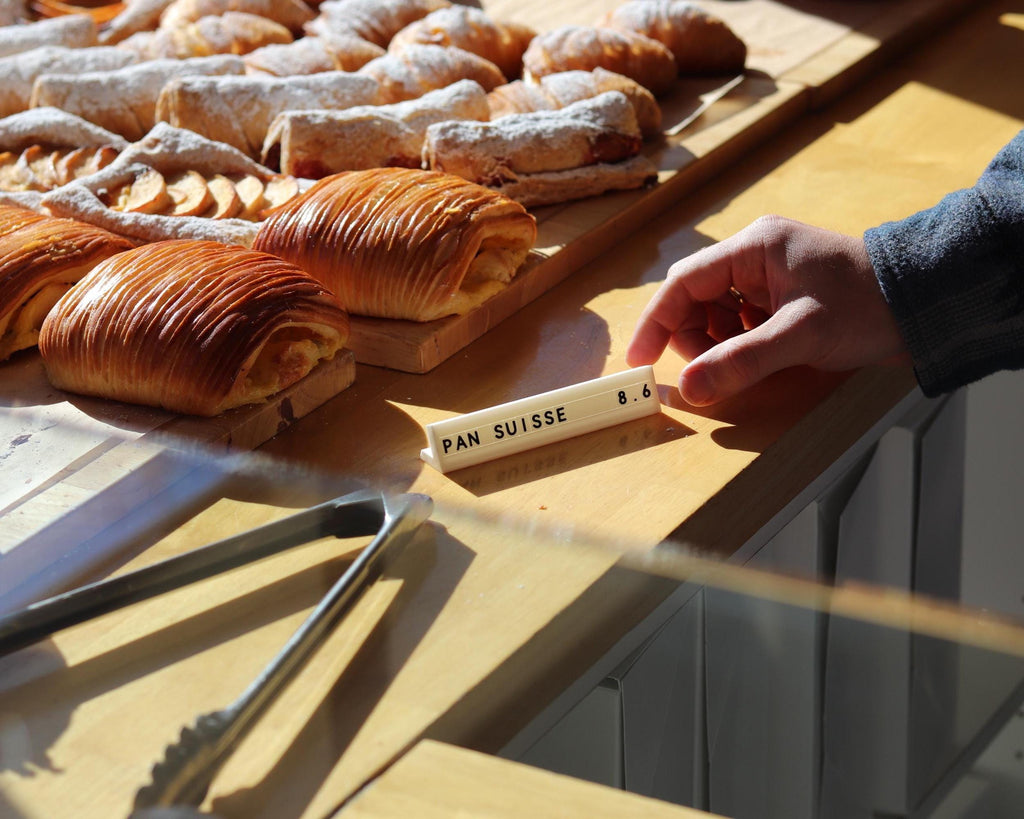 Hand placing a LettrBoard price sign among pastries in a bakery case